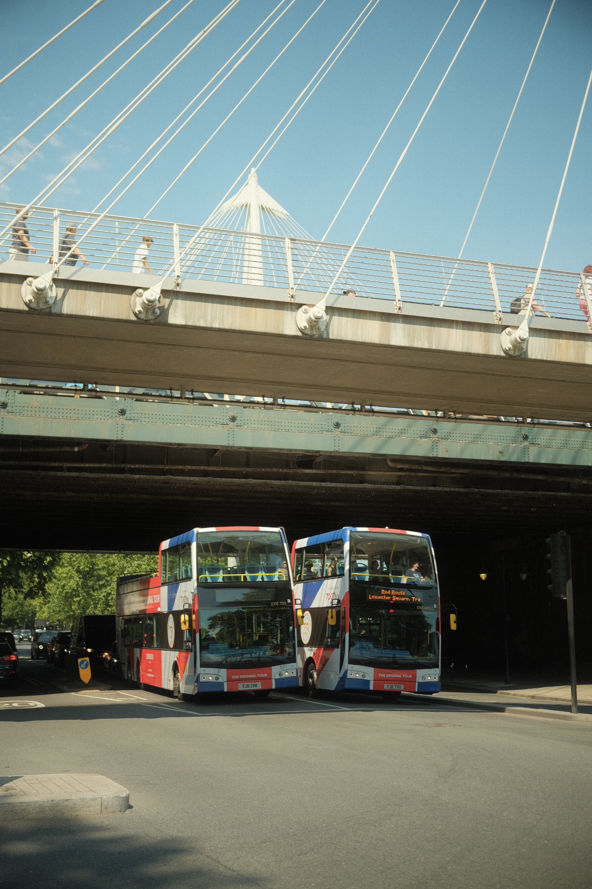 Two double-decker tour buses passing under the Golden Jubilee Bridge, London.
