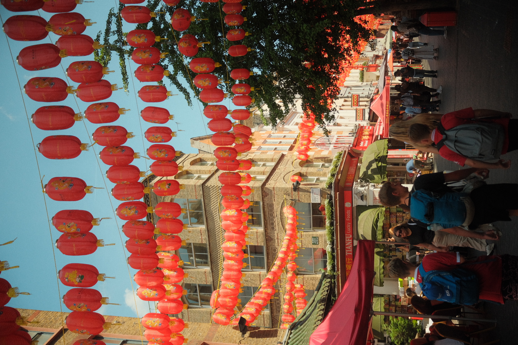 Crowds walking beneath rows of red lanterns in London Chinatown.