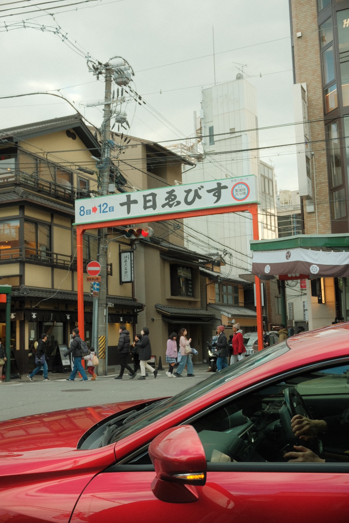Toka Ebisu festival gate over a Kyoto intersection with a red car passing through.