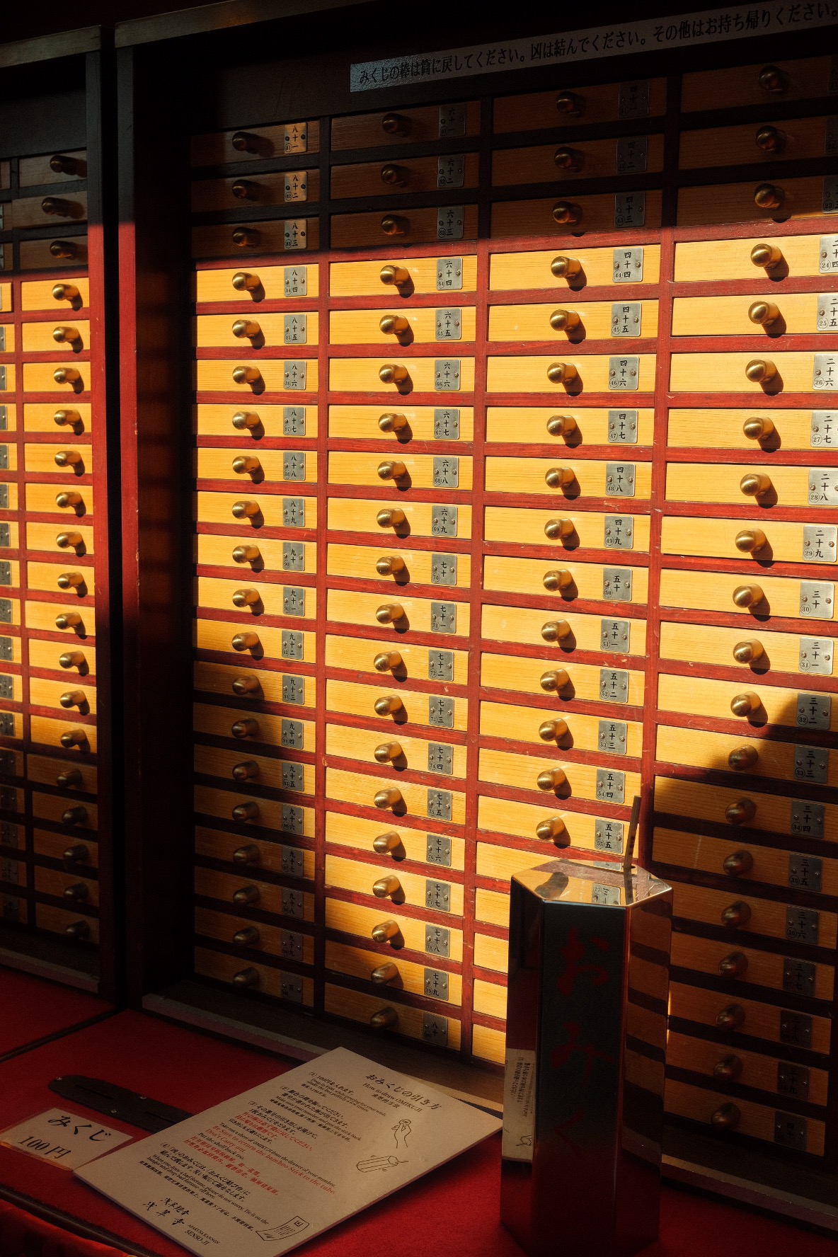 Wall of numbered omikuji fortune drawers glowing at Senso-ji Temple in Tokyo.