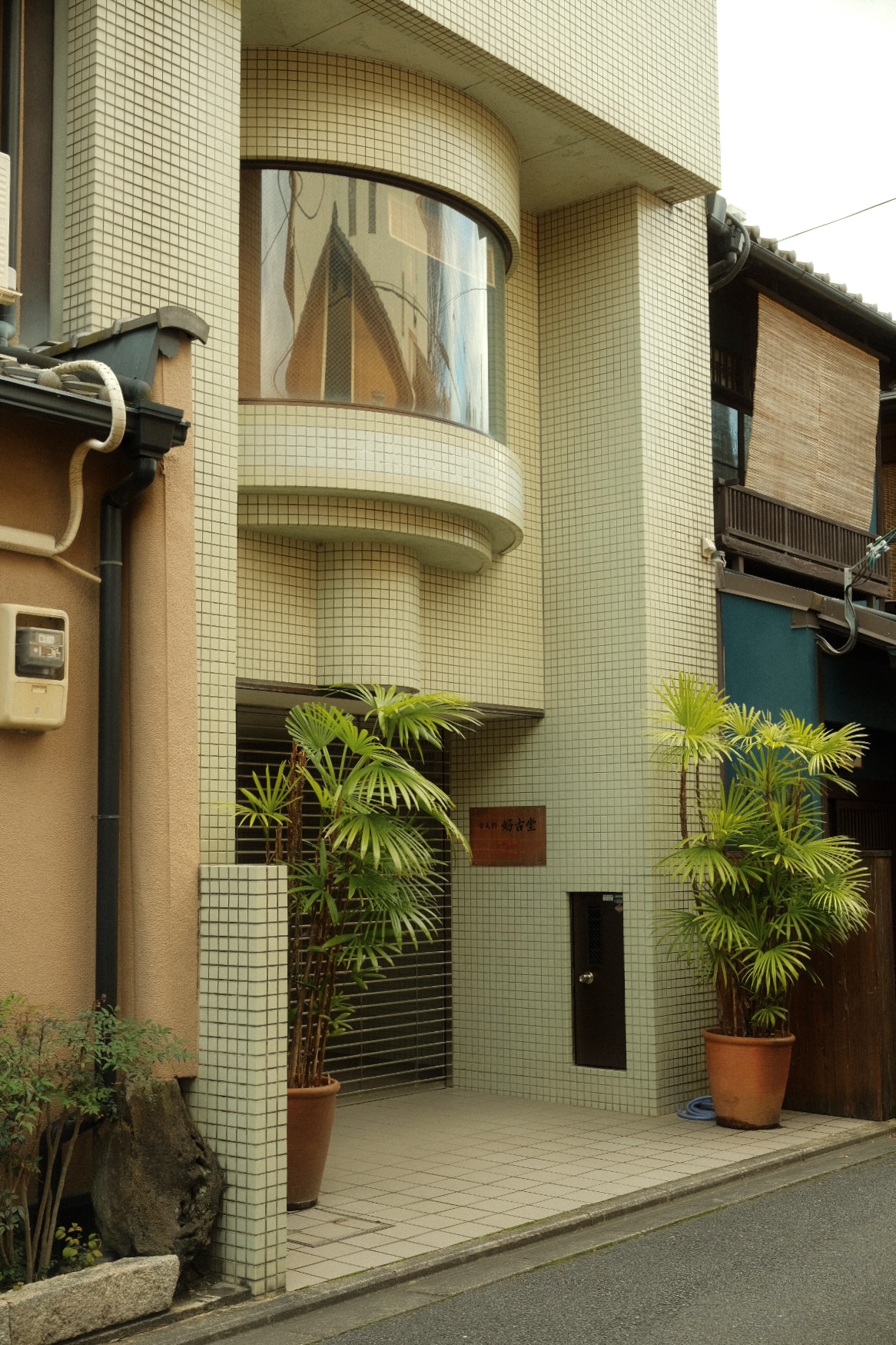 Curved tiled facade of a Kyoto photo studio framed by potted palms on a quiet lane.