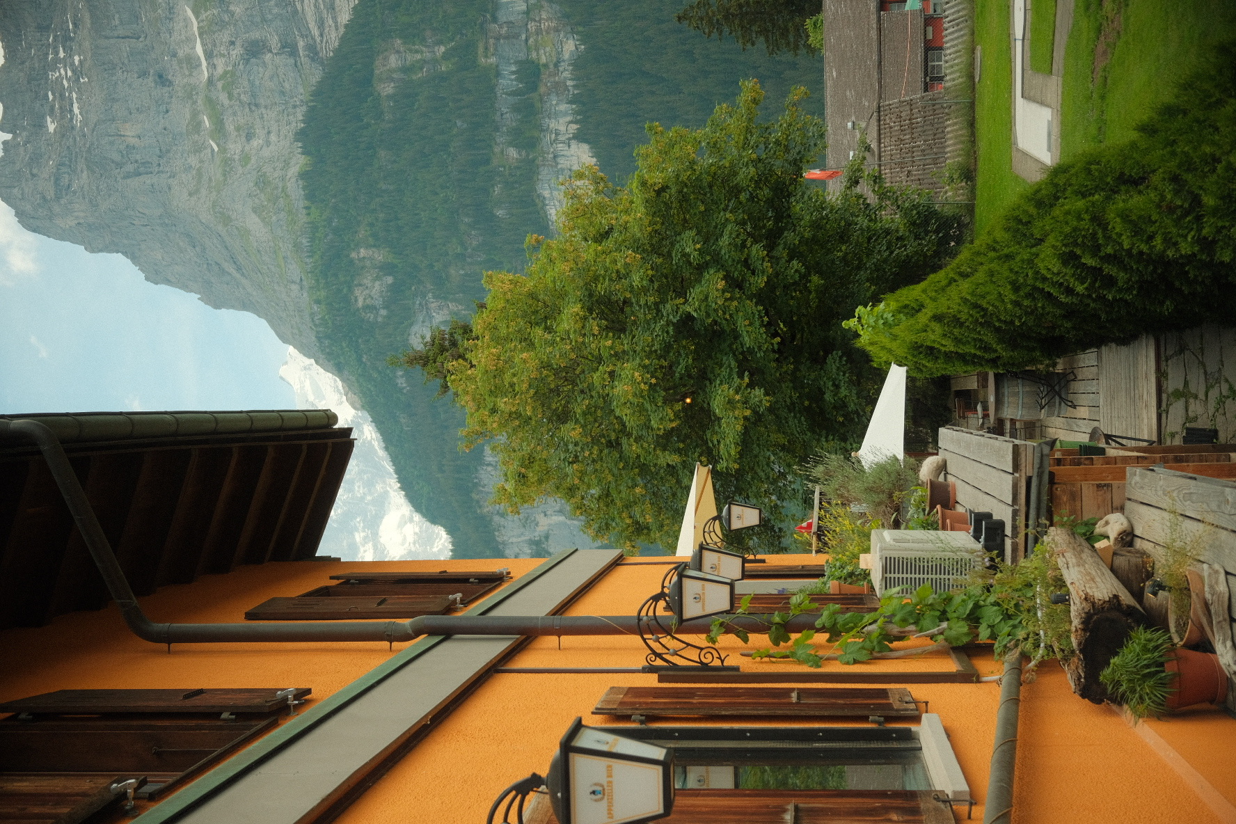 Orange-walled chalet with wooden shutters and terrace lamps below the Lauterbrunnen cliffs.