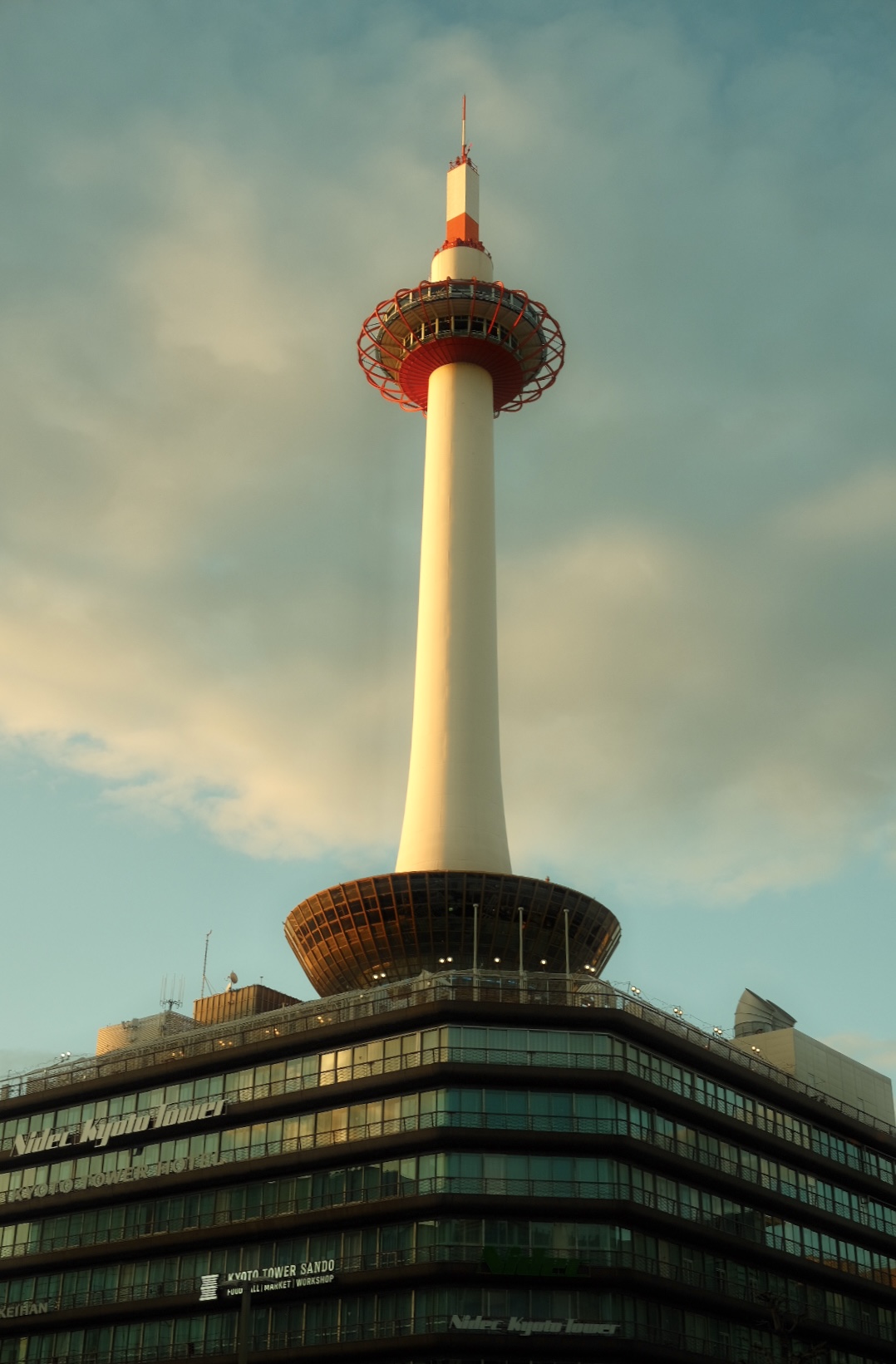 Kyoto Tower glowing above Nidec Kyoto Tower building at golden hour.