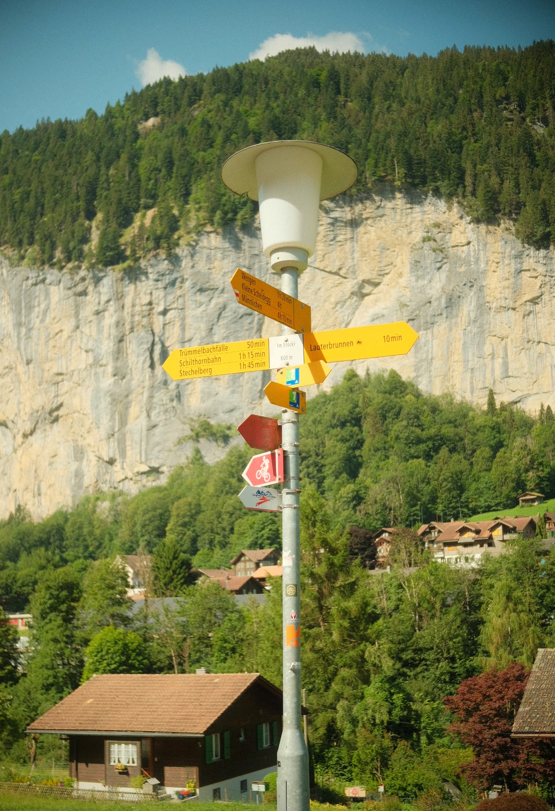Yellow Swiss hiking signpost pointing to Lauterbrunnen and Wengen below sheer valley cliffs.