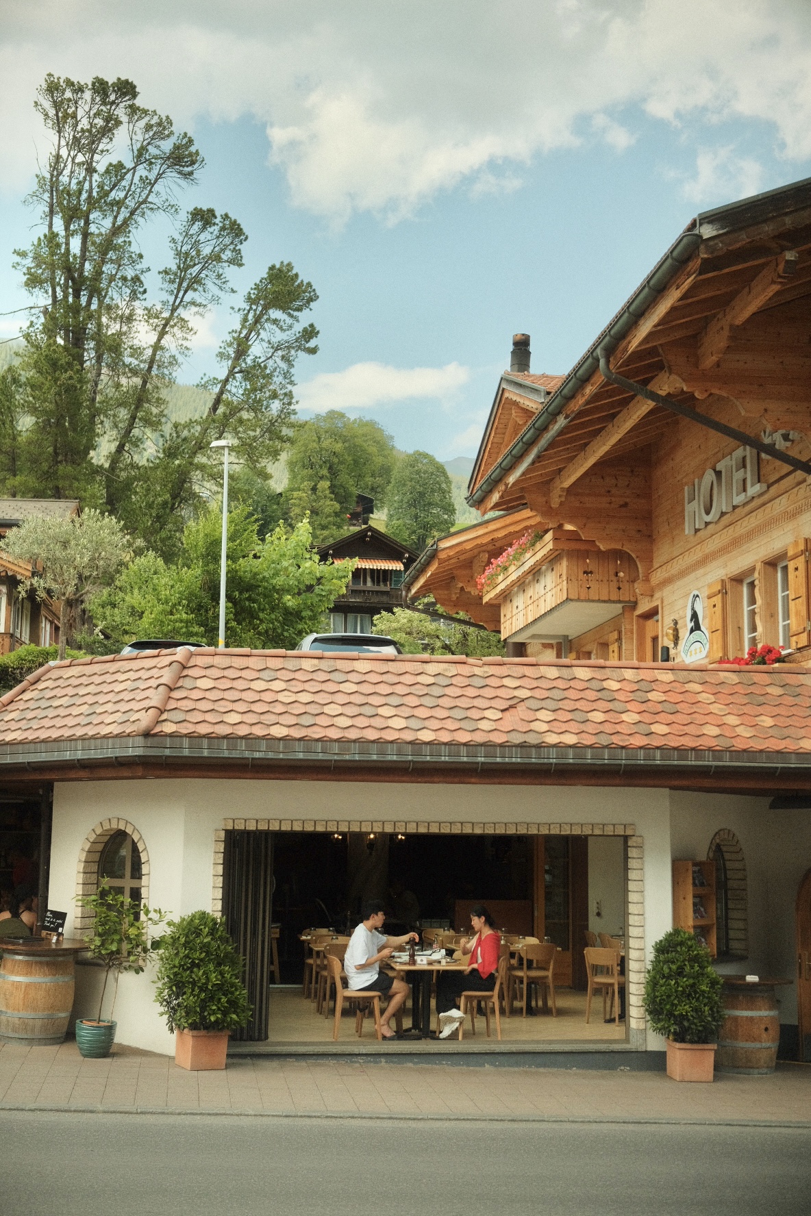 Alpine hotel terrace restaurant with diners under a wooden chalet roof.