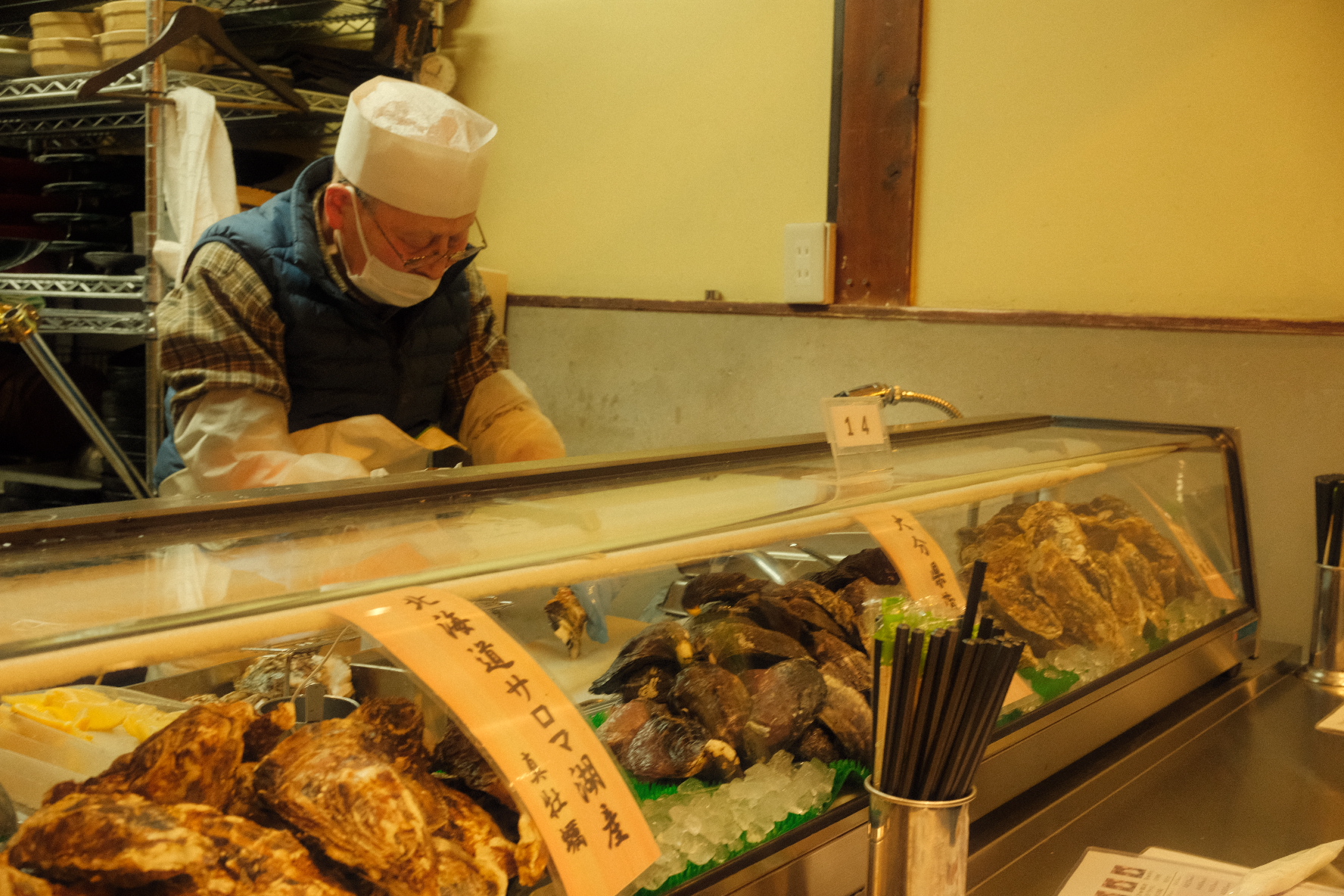 Sushi chef preparing fresh Hokkaido oysters behind a warmly lit counter.