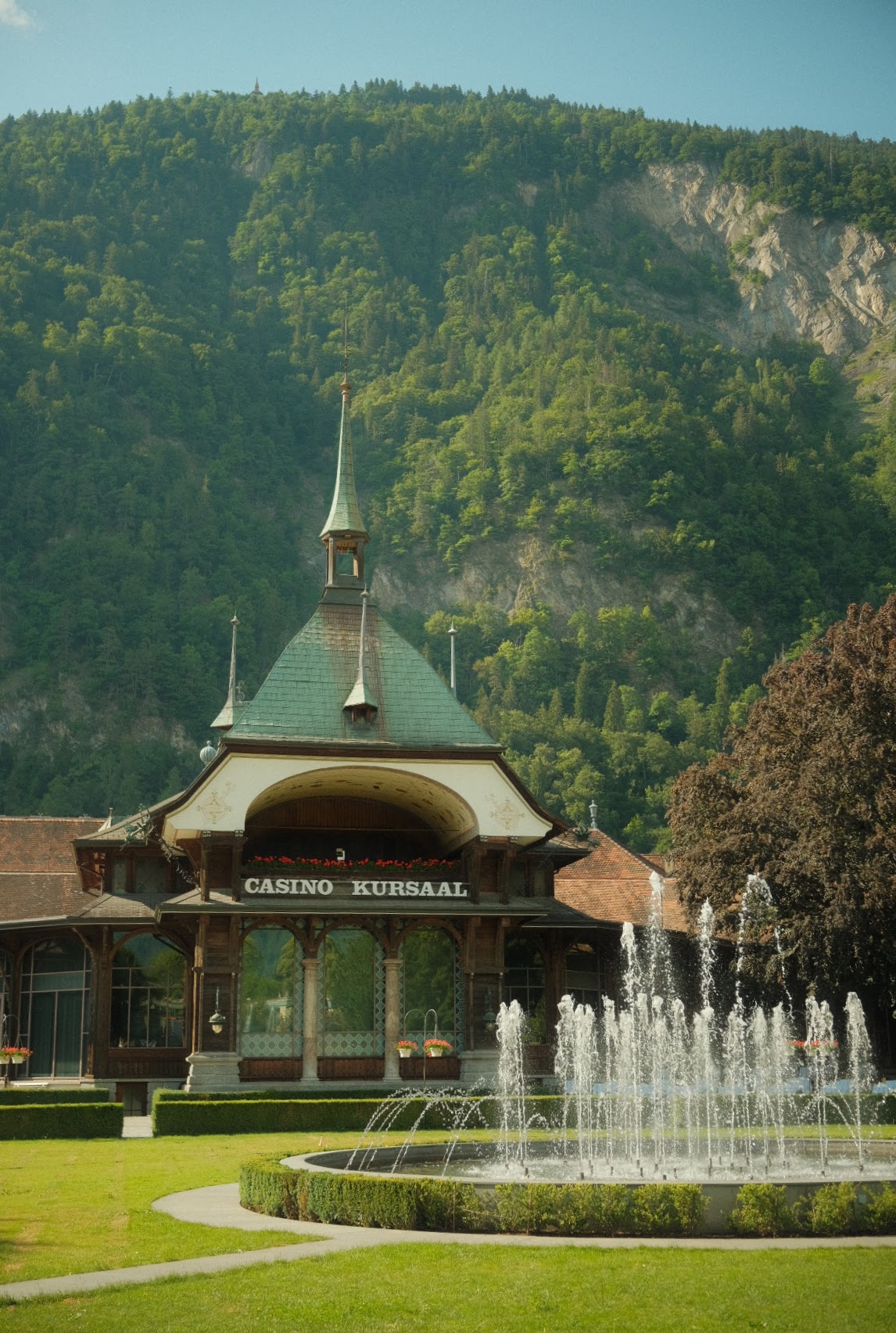Ornate Casino Kursaal pavilion and dancing fountains against a forested mountain in Interlaken.