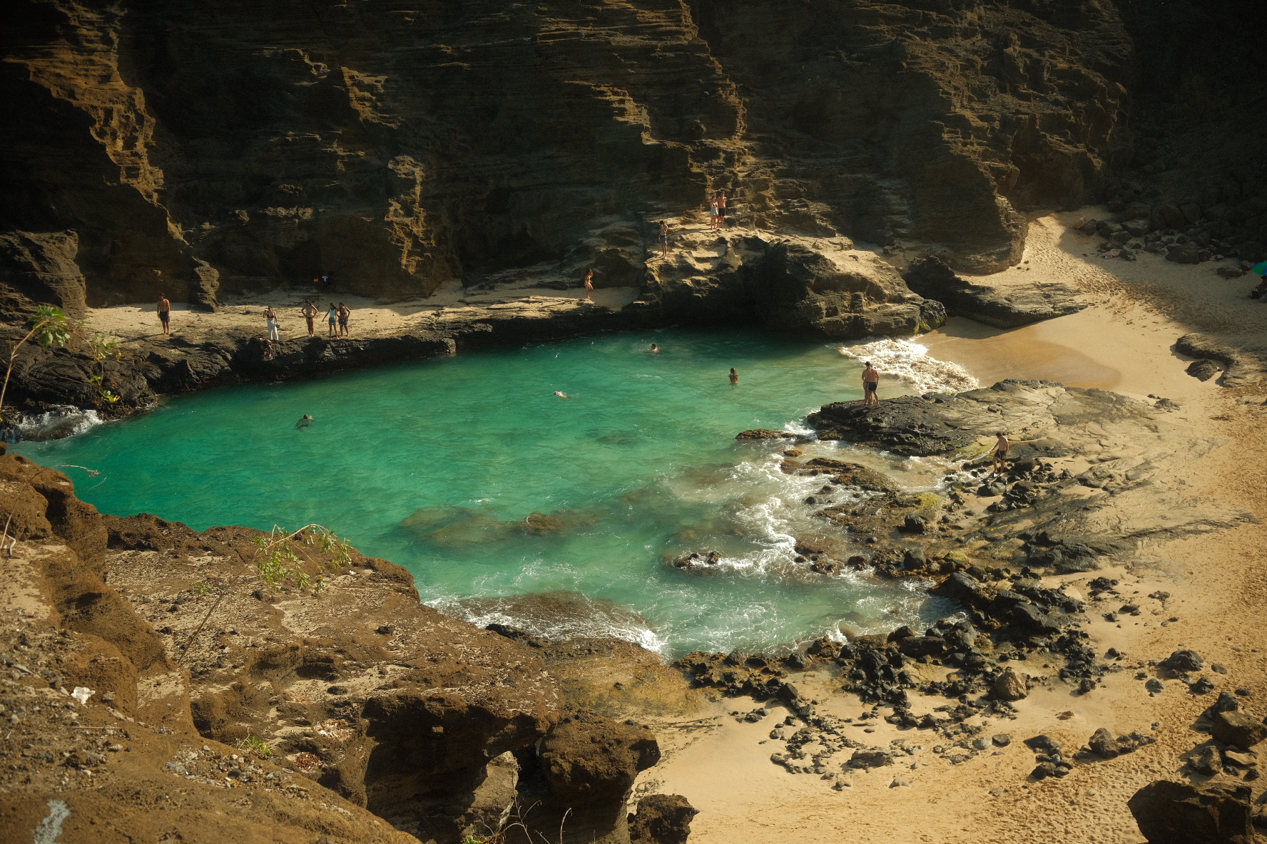 Swimmers in the turquoise water of Halona Cove framed by layered lava-rock cliffs on Oʻahu, Hawaii.