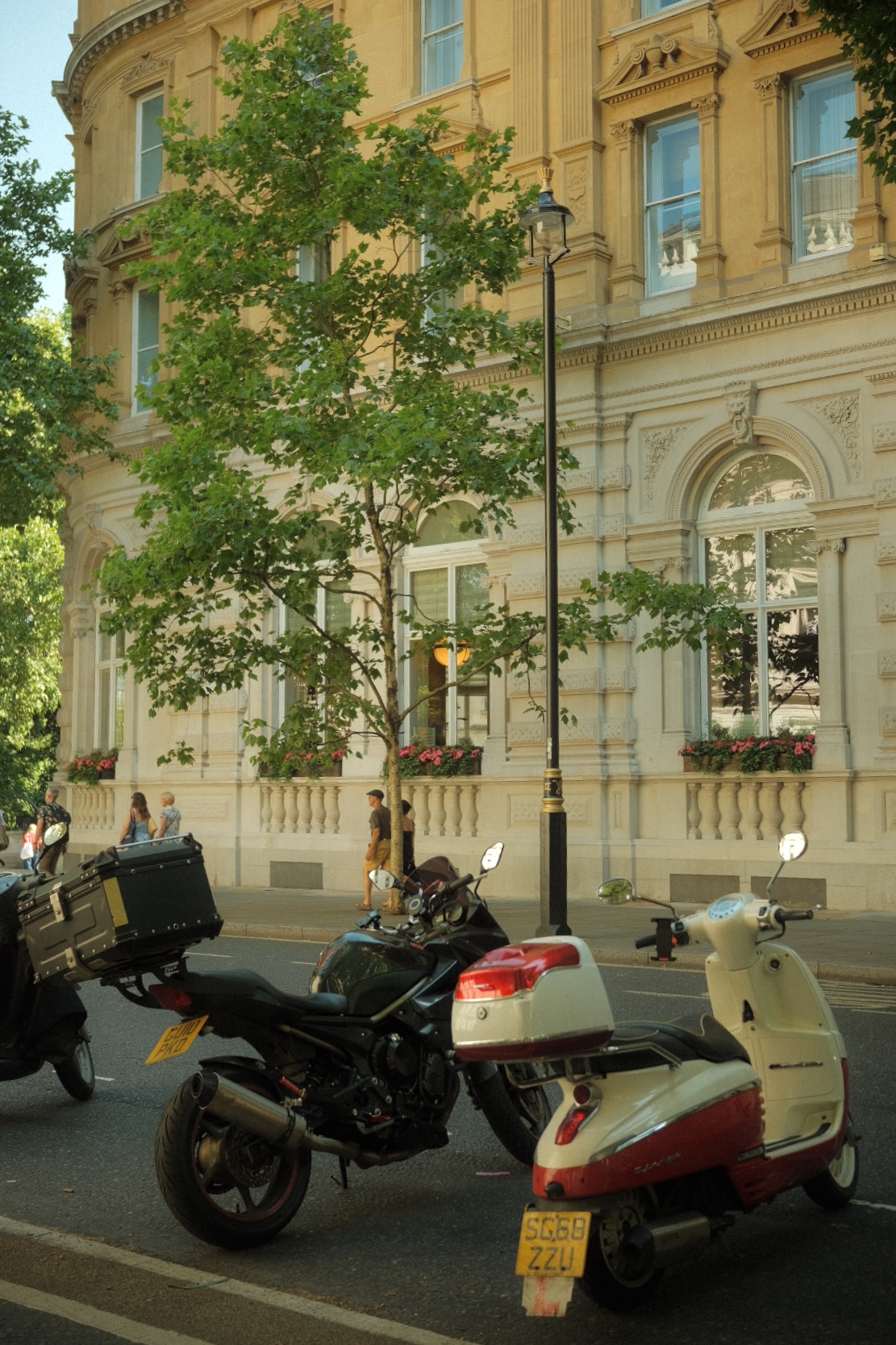Two scooters parked in front of an ornate cream facade in London.