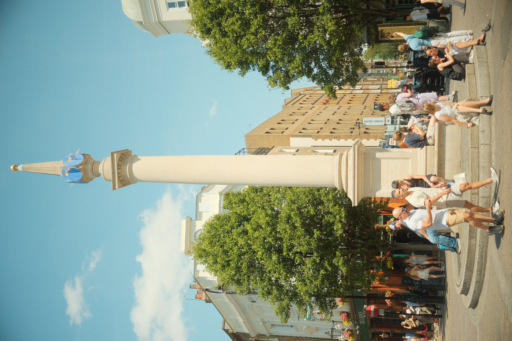 Seven Dials sundial pillar surrounded by people on a sunny day in Covent Garden, London.
