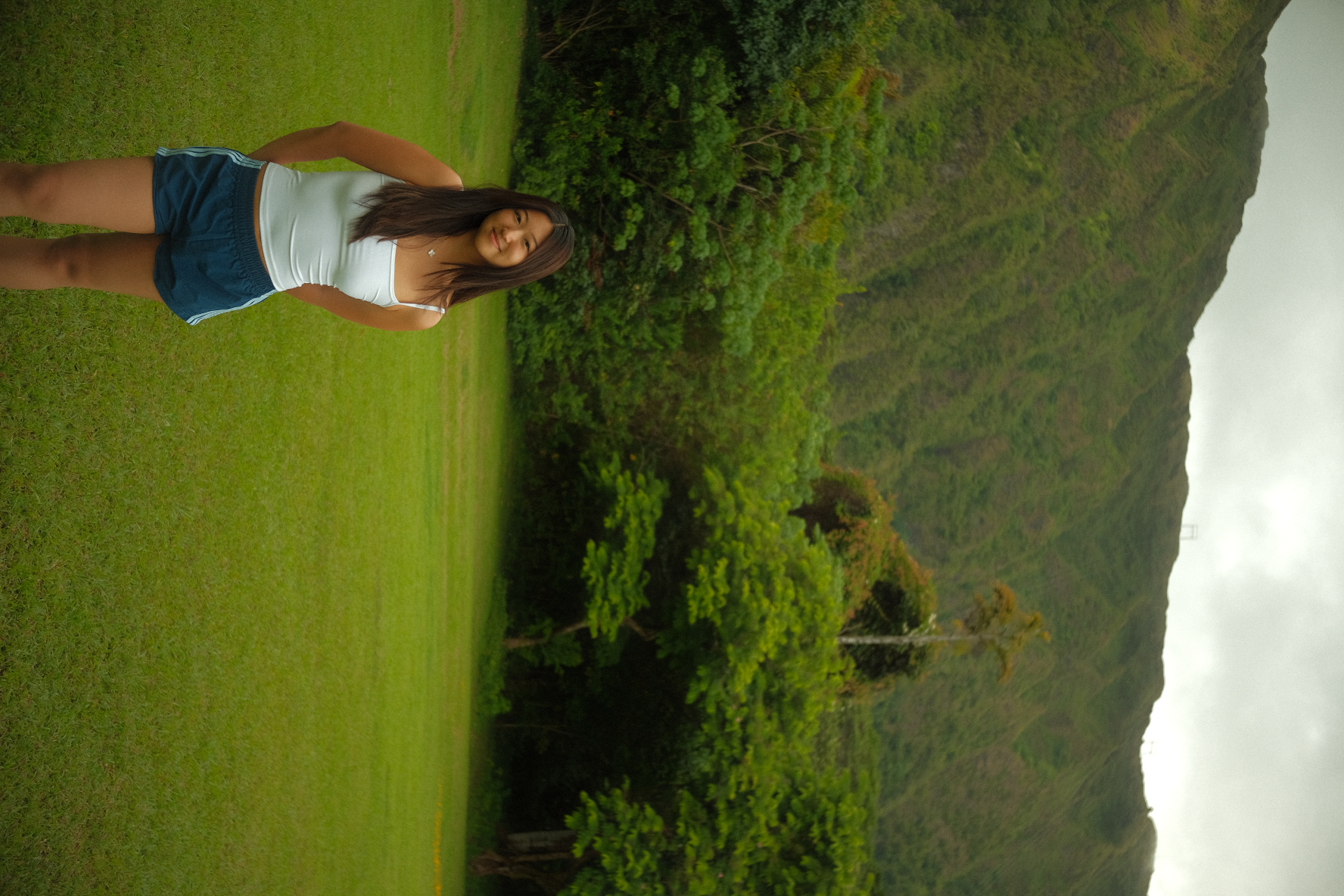 Young woman on a green field with the mist-covered Koʻolau mountains behind her on Oʻahu, Hawaii.