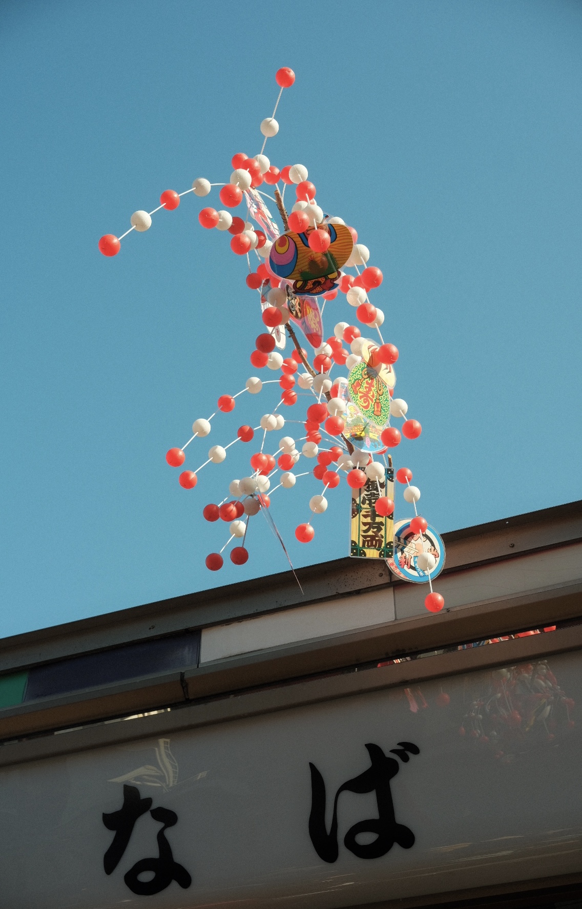 Red and white paper ornaments hanging above a Tokyo shopfront against a blue sky.