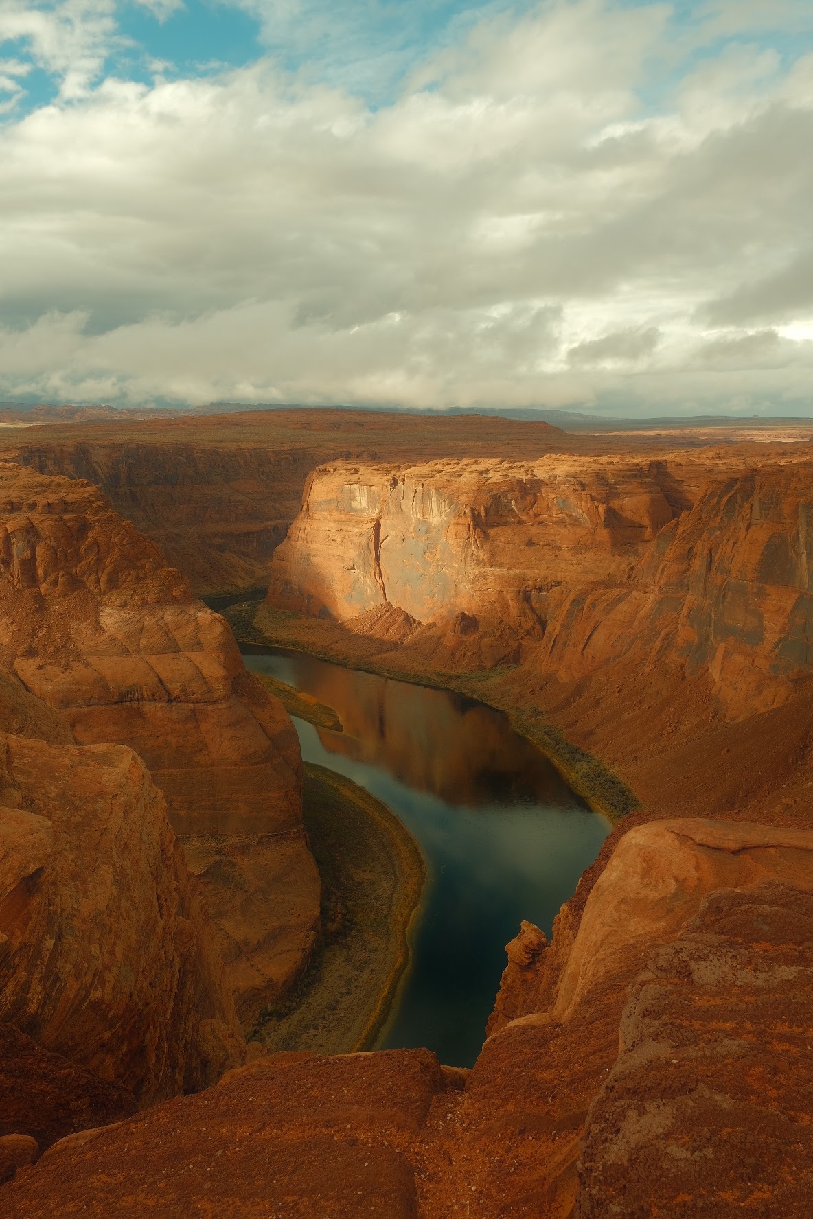 Horseshoe Bend of the Colorado River curving through red-rock canyon walls under a cloudy sky near Page, Arizona.