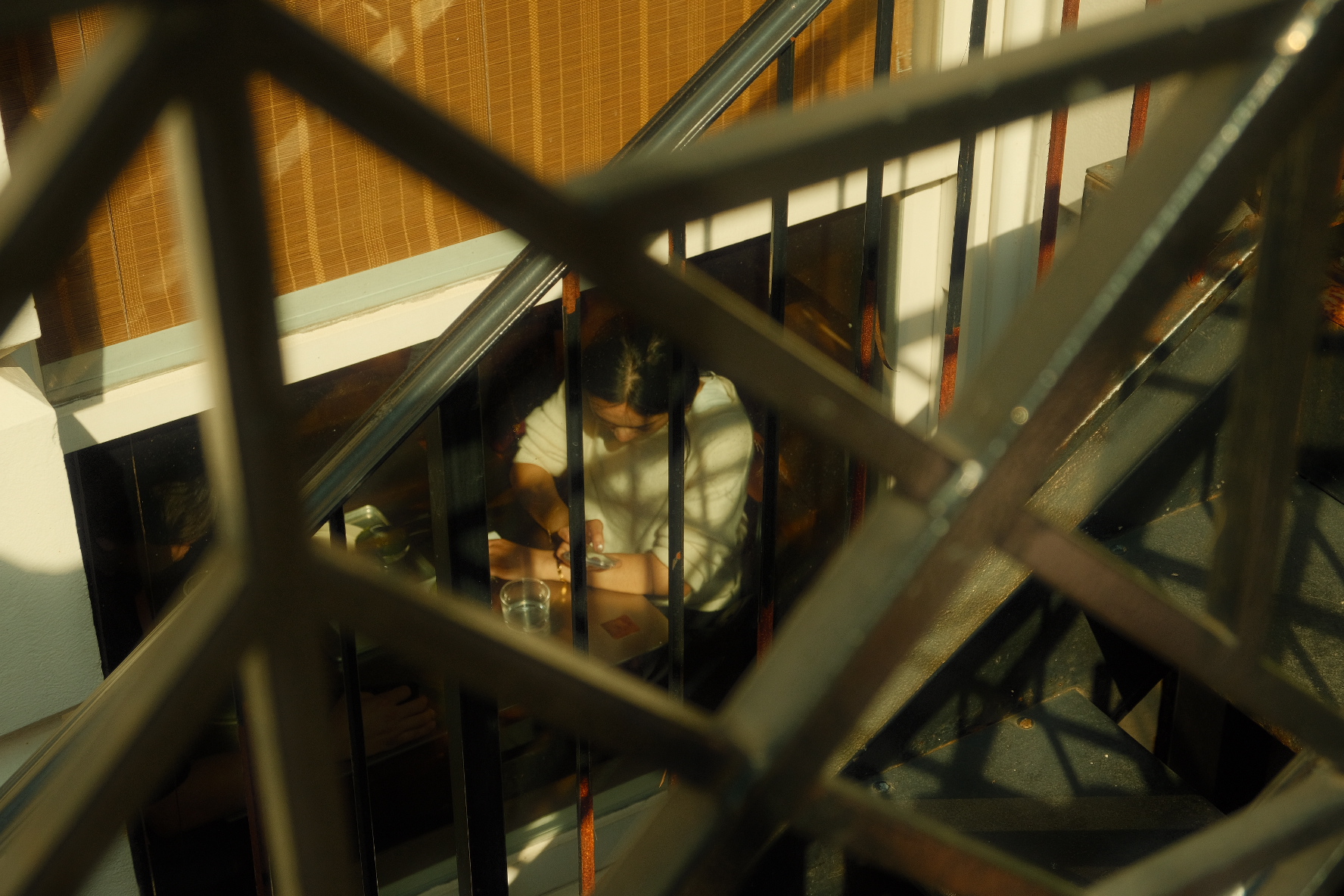 Two people at a café table seen through a black metal railing bathed in golden light, New York.