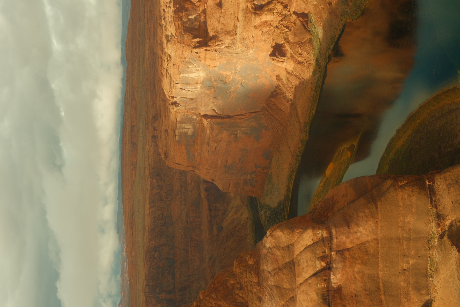 Sunlight raking across the red sandstone walls and river bend of a canyon in Arizona.