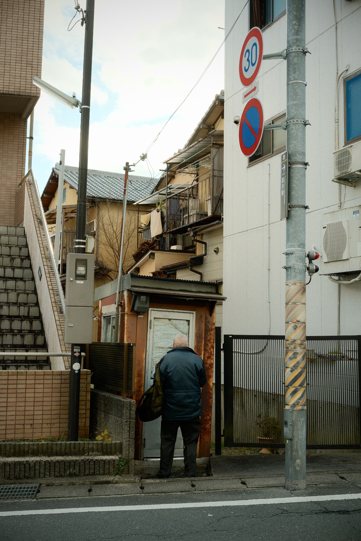 Elderly man pausing at the doorway of a weathered home on a Kyoto side street.