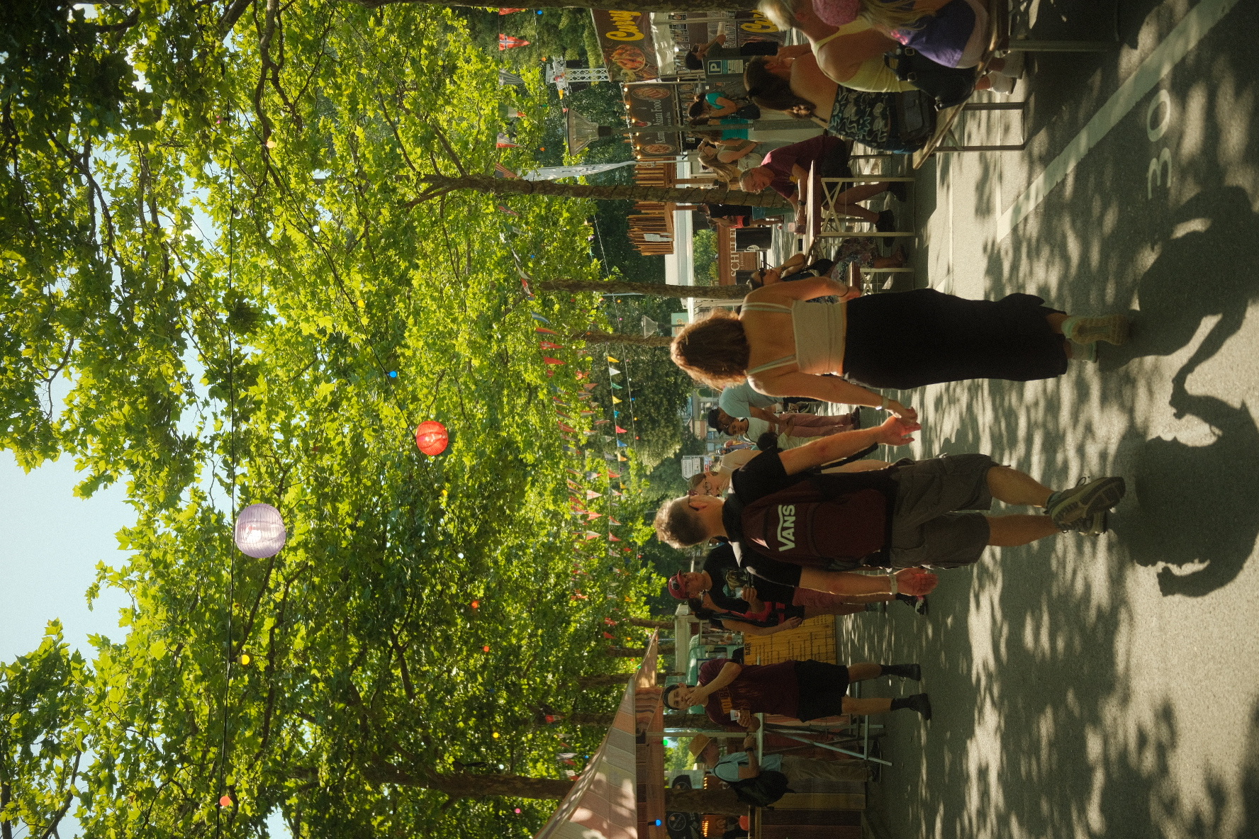 Summer street-food market under leafy trees strung with paper lanterns and bunting in Interlaken.