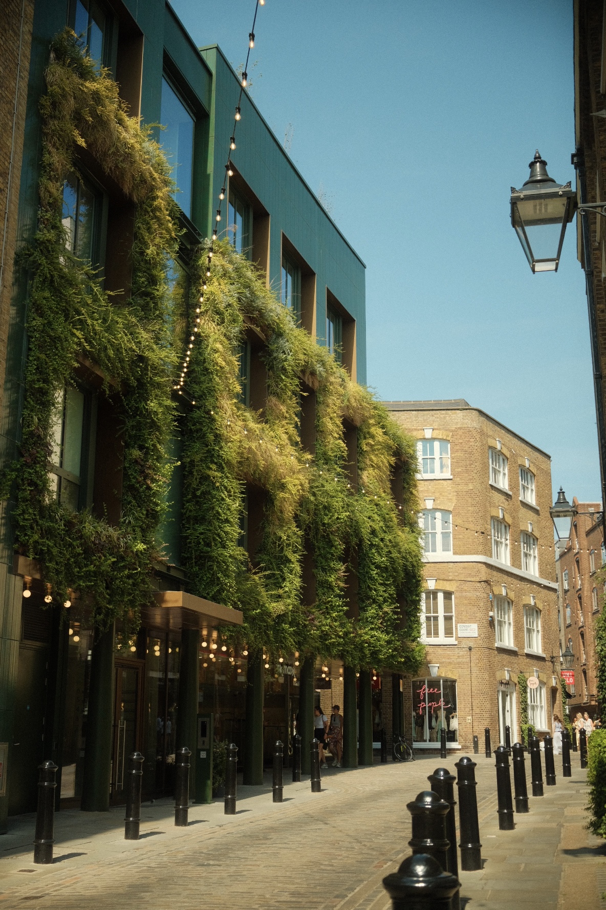 A green ivy-covered modern building along a cobbled London lane.